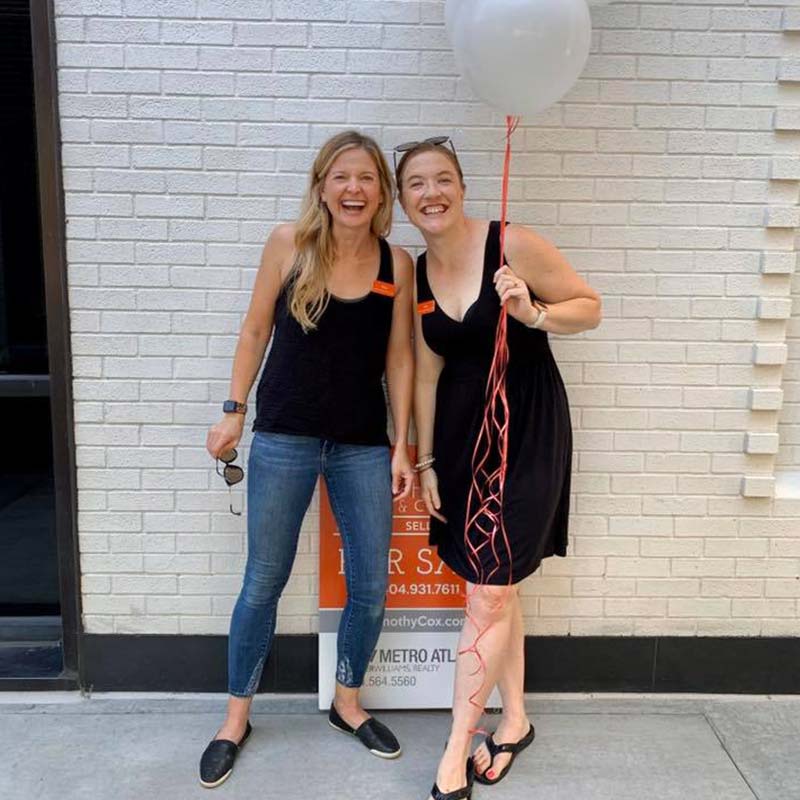 Portrait of Smiling Women Holding a Balloon in Front of a White Brick Walln